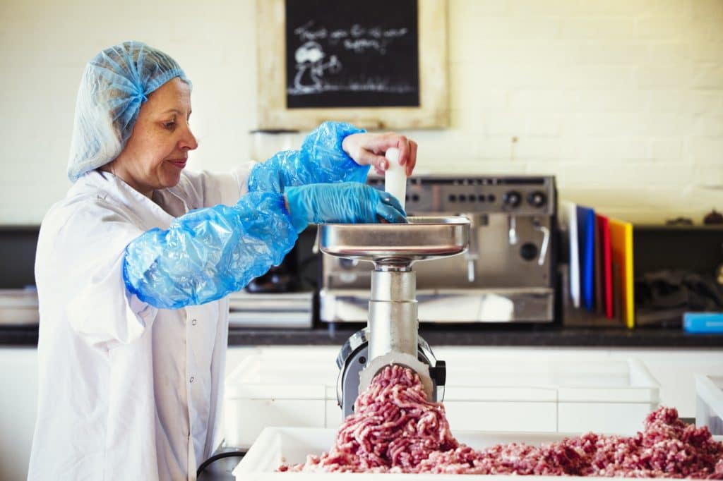 Woman in a butchery putting minced meat into a meat grinder.