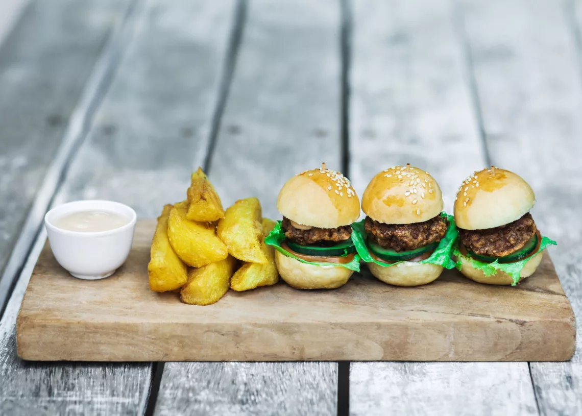 Three Mini Burgers With Beef Patty French Fries And Mayonnaise On Wooden Board
