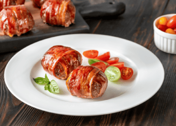2 Bacon Wrapped Paleo Meatballs On A White Plate With Sliced Cherry Tomatoes