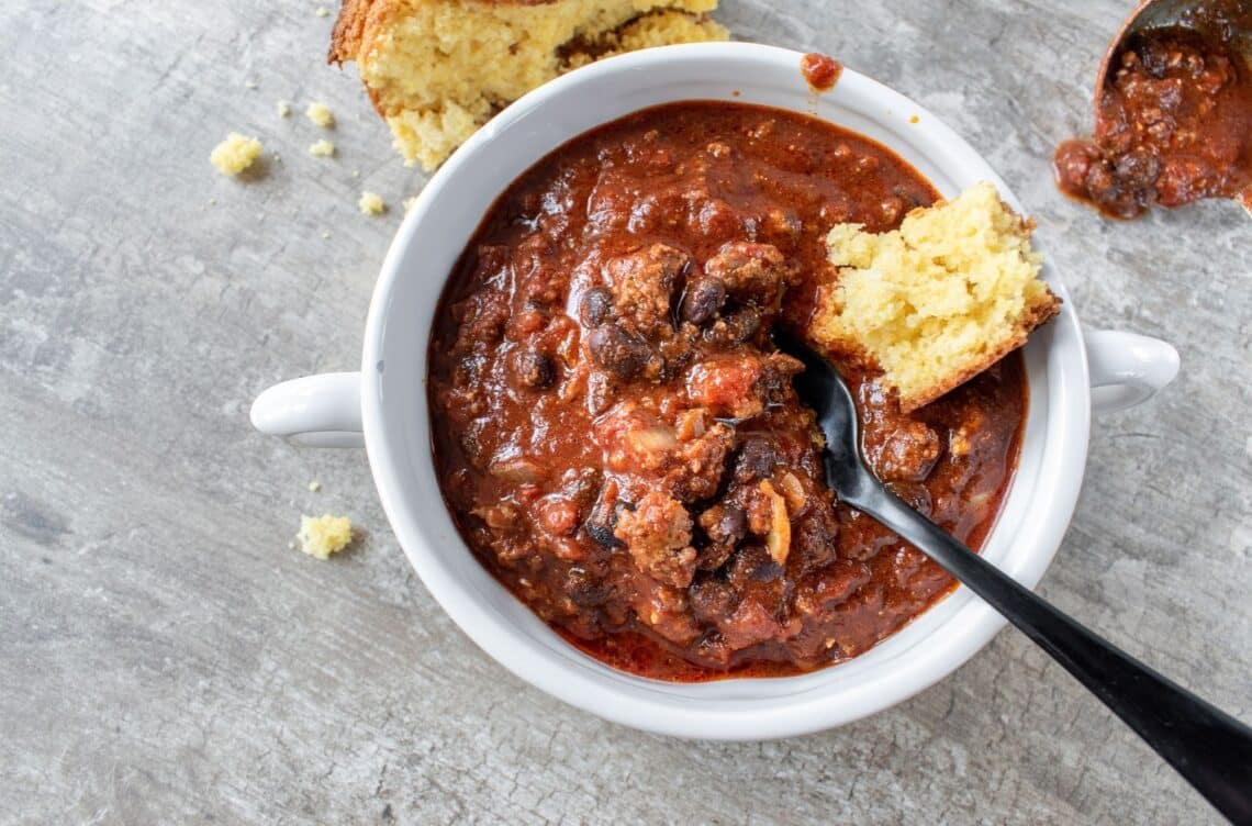 Easy Hearty Beef Chili With Corn Bread On Top In White Bowl
