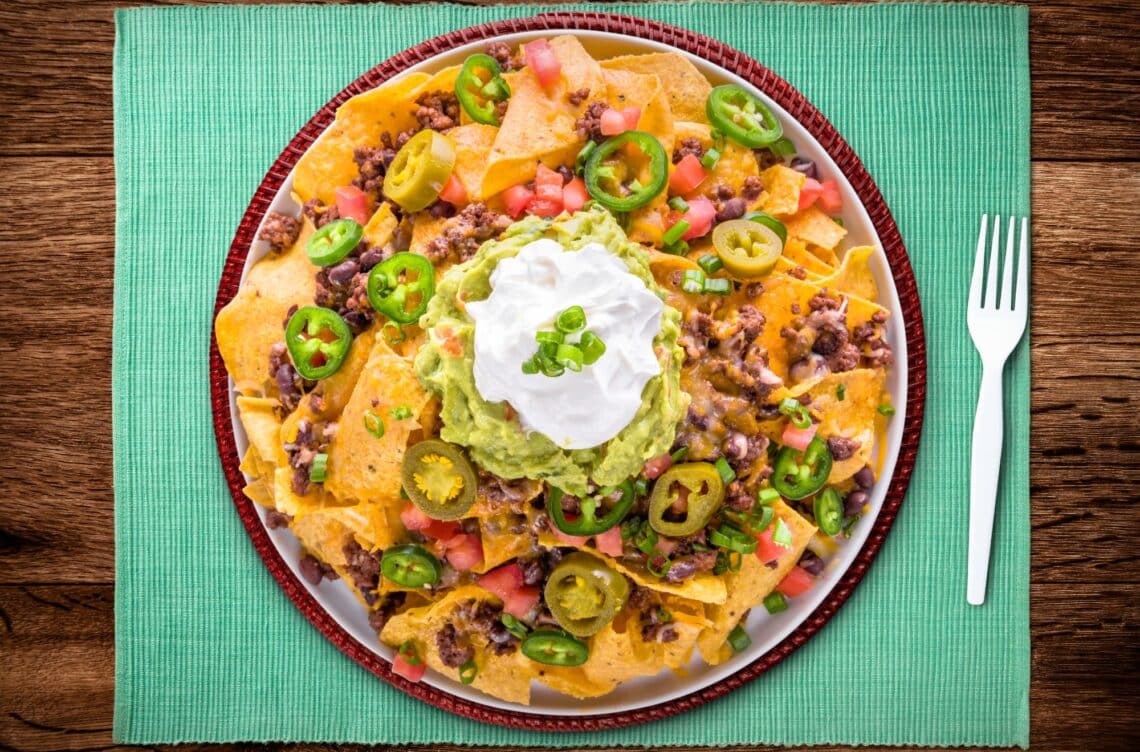 The Best Mexican Chorizo Nachos On A Round Serving Plate With Sour Cream On Top