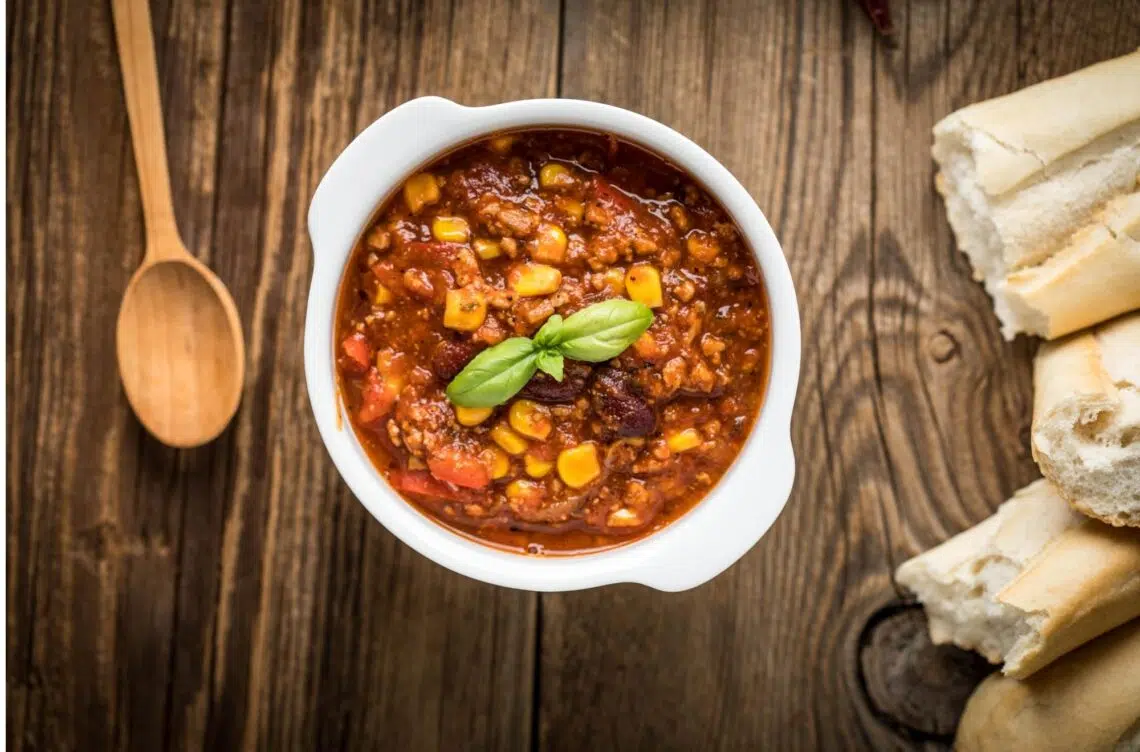 Easy Beef Chili Recipe With Corn In A White Bowl And A Wooden Spoon On The Side