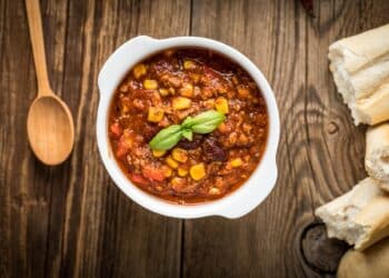 Easy Beef Chili Recipe With Corn In A White Bowl And A Wooden Spoon On The Side