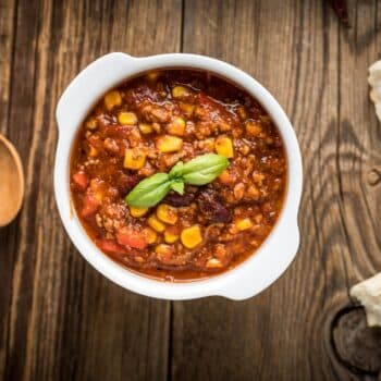 Easy Beef Chili Recipe with Corn In A White Bowl And A Wooden Spoon On The Side