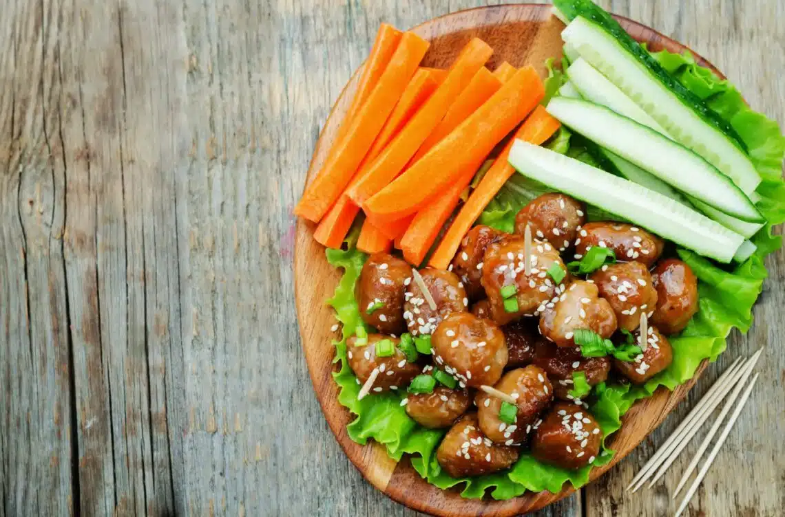 Teriyaki Beef Meatballs On A Wooden Plate With Sliced Carrots And Cucumber
