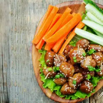 Teriyaki Beef Meatballs On A Wooden Plate With Sliced Carrots And Cucumber